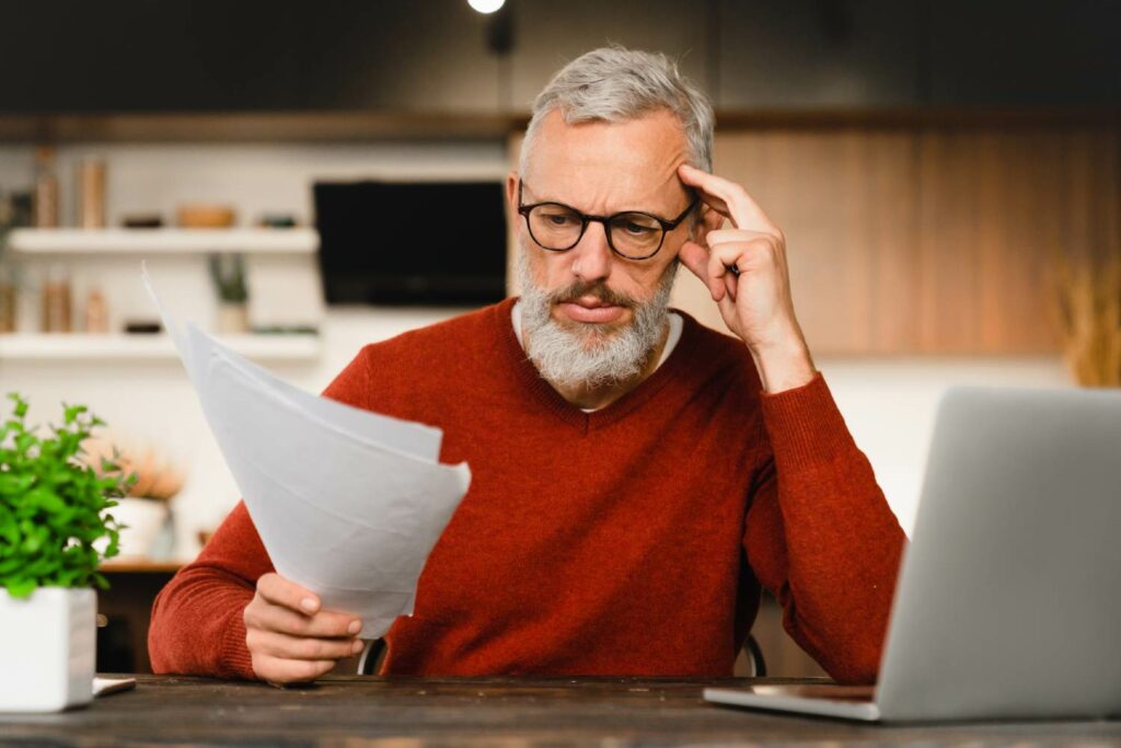 Hombre de mediana edad con barba revisa, preocupado, un documento probablemente de un concurso de acreedores. DCL Gestión